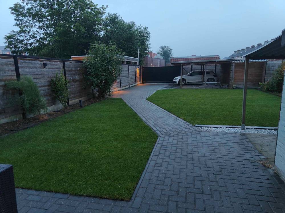 Dezelfde achtertuin na de werken, met een strak gazon en propere randen langs de verharding.