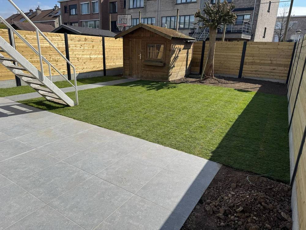 Achtertuin na aanleg met terras, nieuw gazon en houten afsluiting.