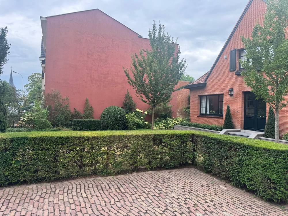 Voortuin met geschoren haag, hortensia's en vormsnoei bij een rode gevel.