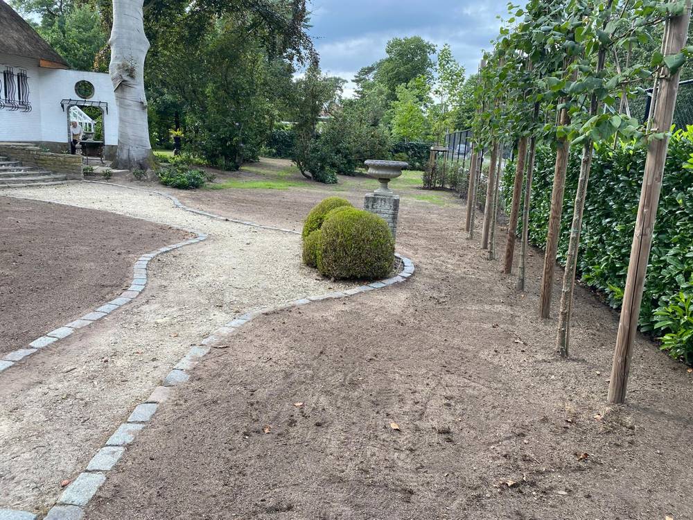 Aanleg van een grindpad met kasseiboorden en jonge leibomen.